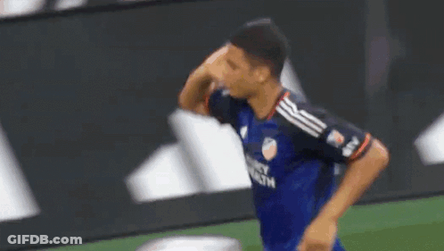 A Soccer Player In A Blue Jersey Is Standing On A Field With His Hand On His Face . GIF