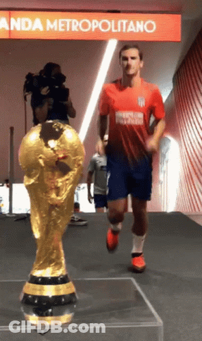 A Soccer Player In A Red And Blue Uniform Is Running Towards A Trophy GIF