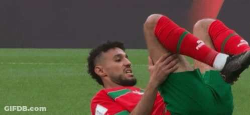 A Soccer Player In A Red And Green Uniform Stretches His Leg GIF