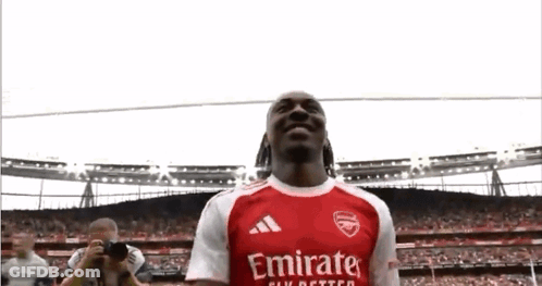 A Soccer Player In A Red And White Emirates Jersey Is Standing In Front Of A Crowd . GIF