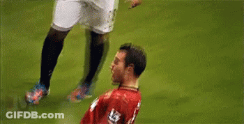 A Soccer Player In A Red Jersey Is Being Tackled By Another Player On A Field . GIF