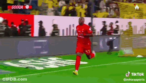 A Soccer Player In A Red Jersey Is Running On The Field With A Crowd Behind Him GIF