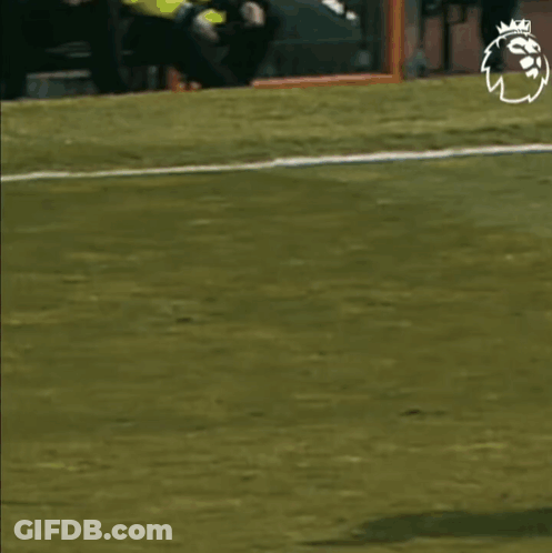 A Soccer Player In A Red Shirt Is Running Towards Another Player In A Black And White Striped Shirt On A Field . GIF