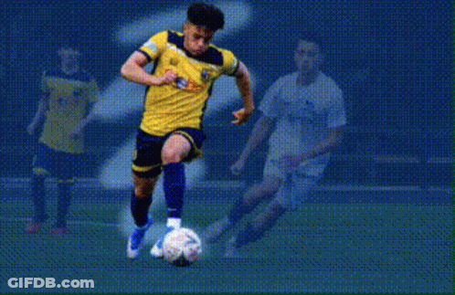 A Soccer Player In A Yellow And Blue Jersey Is Dribbling A Soccer Ball With The Word Fields Behind Him GIF