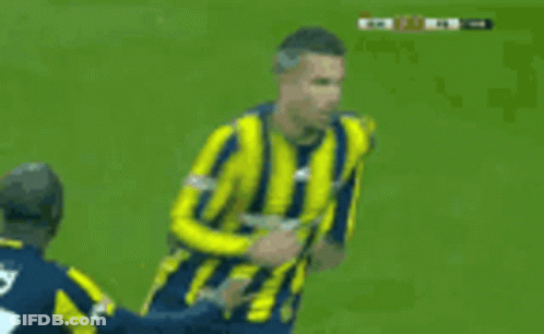 A Soccer Player In A Yellow And Blue Striped Jersey Is Being Tackled By Another Player GIF