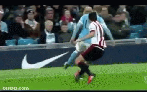 A Soccer Player Is Being Tackled By Another Player On A Soccer Field . GIF