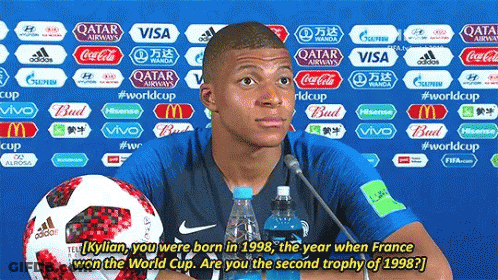 A Soccer Player Is Giving A Press Conference With A Bottle Of Water And A Soccer Ball Behind Him GIF