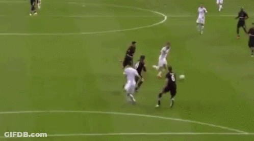 A Soccer Player Is Jumping In The Air To Score A Goal While A Goalkeeper Is Laying On The Field . GIF