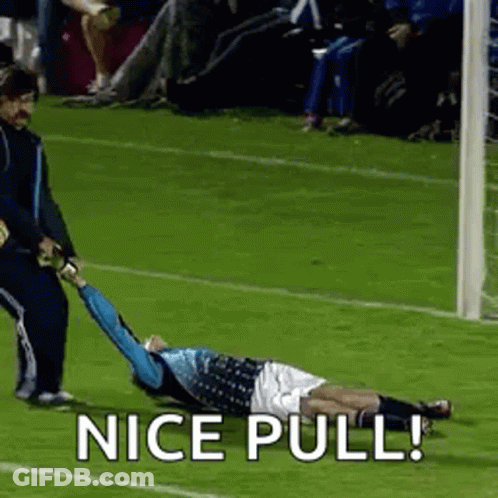 A Soccer Player Is Laying On The Ground While A Referee Pulls Him To The Goal . GIF