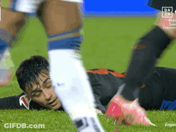 A Soccer Player Is Laying On The Ground While Another Player Kicks Him GIF