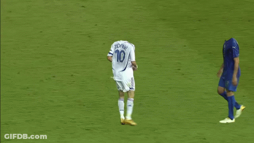 A Soccer Player Is Laying On The Ground While Another Player Runs Towards Him GIF