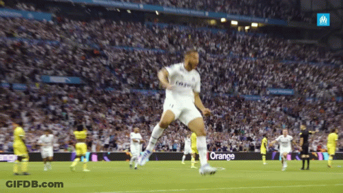 A Soccer Player Jumps In The Air In Front Of A Crowd With An Orange Sign In The Background GIF