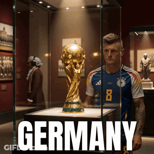 A Soccer Player Stands In Front Of A Fifa Trophy In A Glass Case GIF