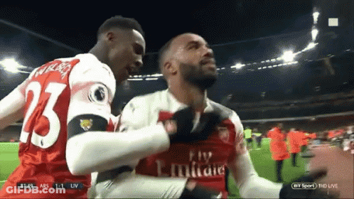 A Soccer Player Wearing A Fly Emirates Jersey Is Being Hugged By Another Player GIF