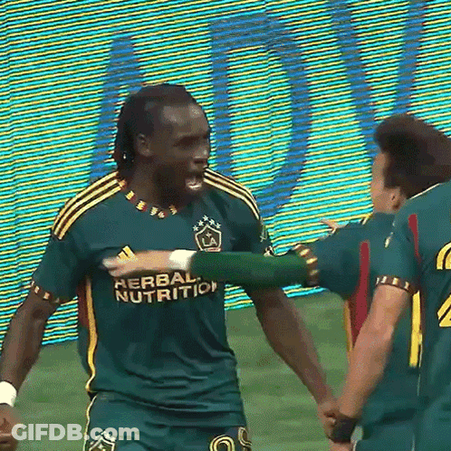 A Soccer Player Wearing A Green Herbal Nutrition Jersey Is Hugging Another Player GIF