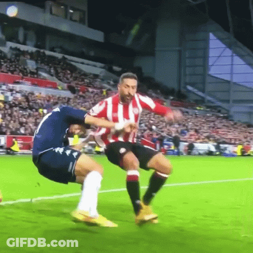 A Soccer Player Wearing A Red And White Striped Shirt Is Being Tackled By Another Player GIF