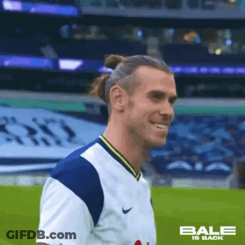 A Soccer Player Wearing A White And Blue Jersey Is Smiling On A Field . GIF