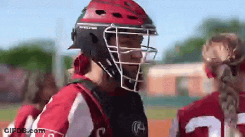A Softball Player Wearing A Helmet And A Catcher 'S Mask Is Talking To Another Player On The Field . GIF