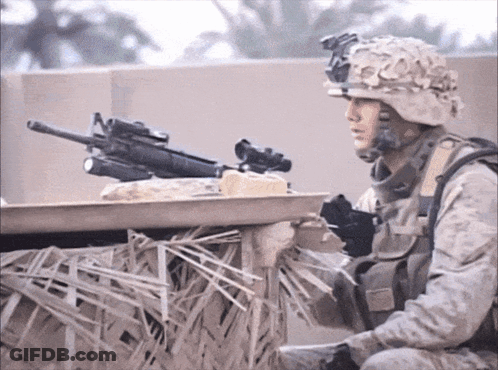 A Soldier In A Helmet Holds A Gun In His Right Hand GIF