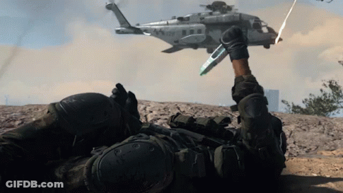 A Soldier Laying On The Ground With A Helicopter Flying In The Background With The Letters Usmc On It GIF