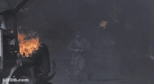 A Soldier Stands In Front Of A Truck That Is On Fire GIF