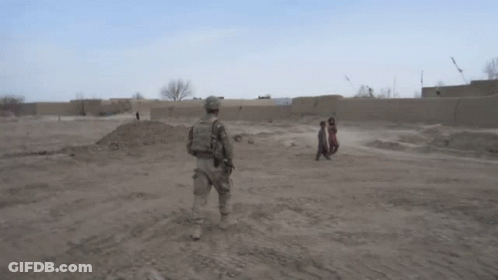 Soldier In Field With Children Walking Behind GIF