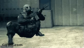 A Soldier Wearing A Gas Mask Is Holding A Gun While Sitting On The Ground . GIF