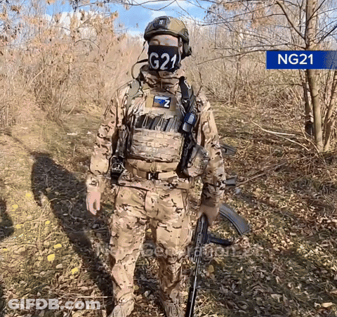 A Soldier Wearing A Mask With G21 On It Stands In The Woods GIF