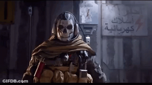 A Soldier With A Skull On His Head Is Standing In Front Of A Wall With Arabic Writing GIF
