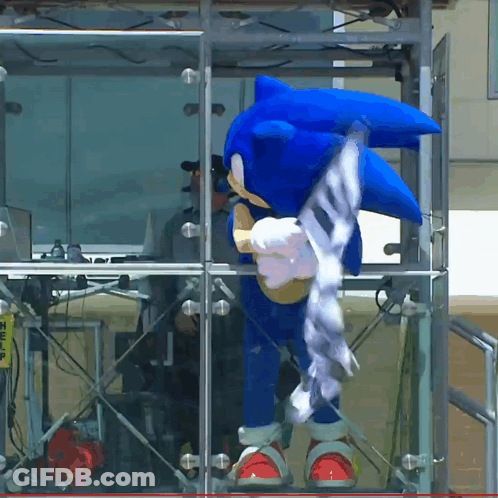 A Sonic The Hedgehog Costume Is Standing In Front Of A Glass Wall GIF