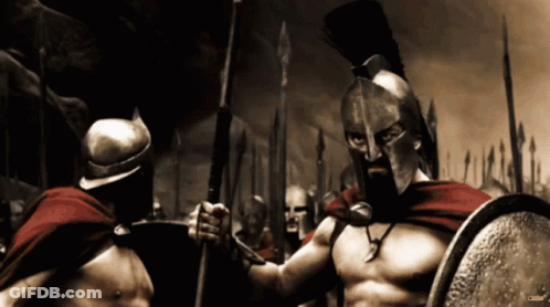 A Spartan Soldier Is Holding A Spear And Shield While Standing Next To Another Spartan Soldier GIF
