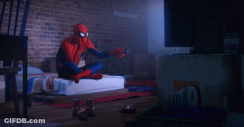 A Spider Man Is Sitting On A Bed Holding A Remote Control GIF