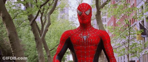 A Spider Man Is Standing In Front Of Trees And Buildings GIF