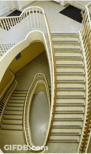 A Spiral Staircase With A White Railing And A Black Mat On The Ground GIF