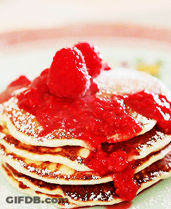 A Stack Of Pancakes Topped With Raspberries And Powdered Sugar GIF