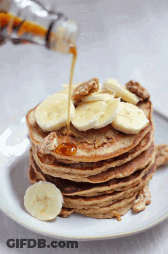 A Stack Of Pancakes With Bananas And Walnuts Being Poured Syrup On Top GIF