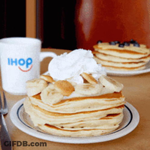 A Stack Of Pancakes With Bananas And Whipped Cream On A Plate Next To An Ihop Mug GIF