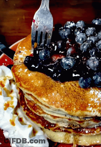 A Stack Of Pancakes With Blueberries On Top And Whipped Cream On The Side GIF