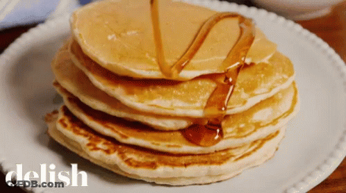 A Stack Of Pancakes With Syrup Being Poured On Them Is On A White Plate With The Word Delish On It GIF