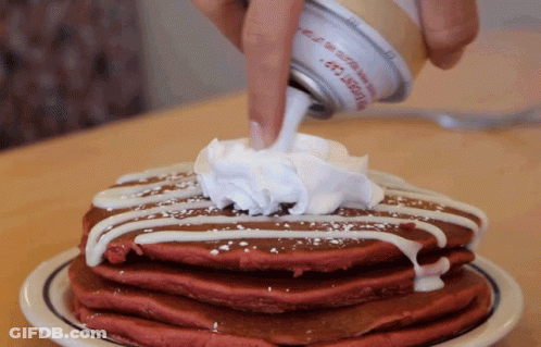 A Stack Of Red Velvet Pancakes With Whipped Cream Being Poured On Top GIF