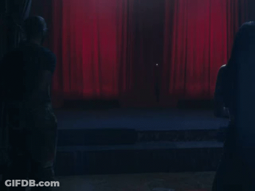 A Stage With A Red Curtain And A Few People Watching GIF