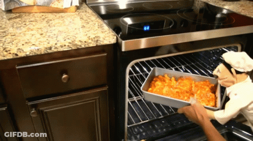 A Statue Of A Chef Is Holding A Pan Of Food In An Oven GIF