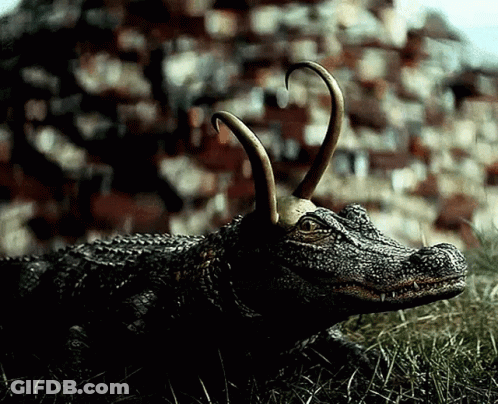 A Statue Of A Crocodile With Horns Is Laying In The Grass GIF