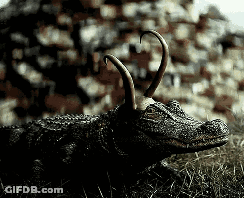 A Statue Of A Crocodile With Horns Laying In The Grass GIF