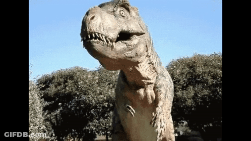 A Statue Of A Dinosaur Is Standing In Front Of Some Trees GIF