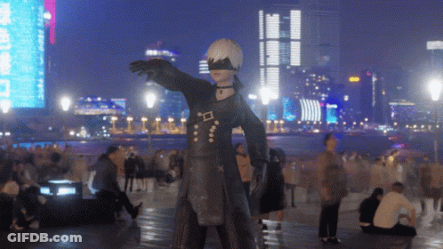 A Statue Of A Man In A Black Suit Is Standing In Front Of A City Skyline At Night GIF