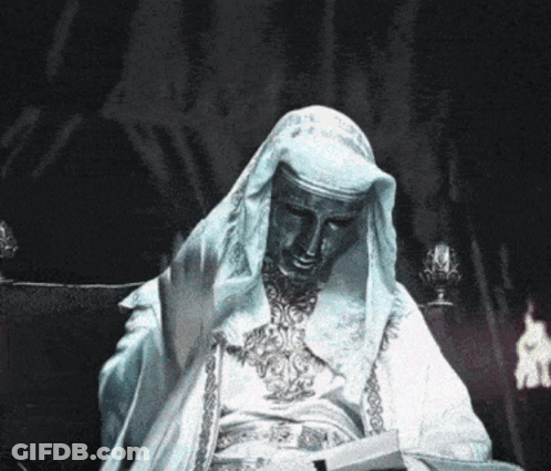 Statue Of Man In White Robe Sitting In Dark Room GIF