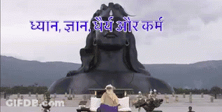 A Statue Of A Man Sitting In Front Of A Large Statue Of A Man GIF