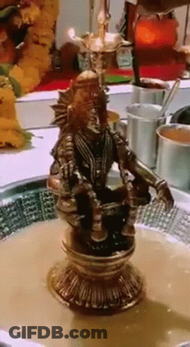 A Statue Of A Man Sitting On A Pedestal With A Bowl Of Liquid In Front Of Him GIF