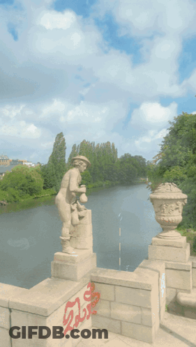 A Statue Of A Man Standing Next To A Body Of Water With Graffiti On The Wall That Says ' Shaolia ' GIF